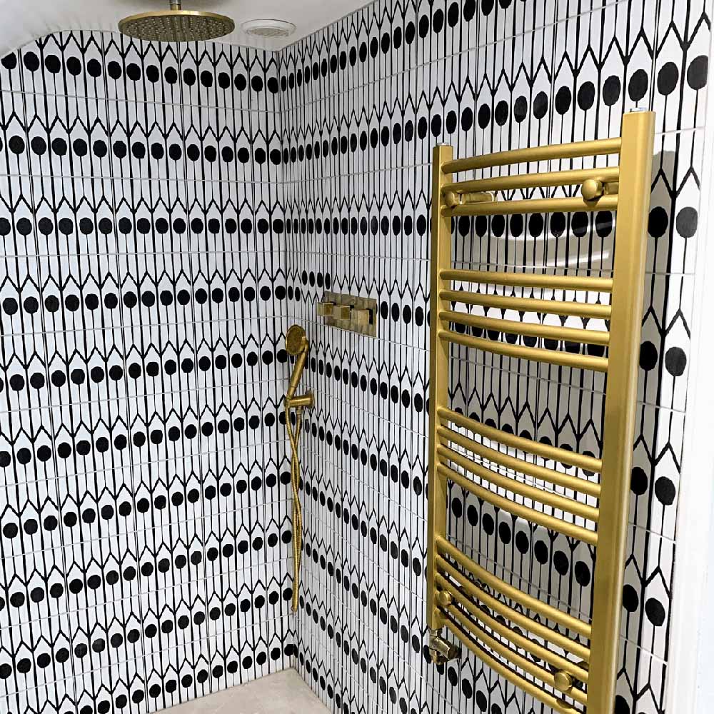 Shower area featuring Almeria Felis Moroccan-style porcelain wall tiles in a bold black and white geometric dot and line pattern, 20x20cm, paired with brass fixtures.