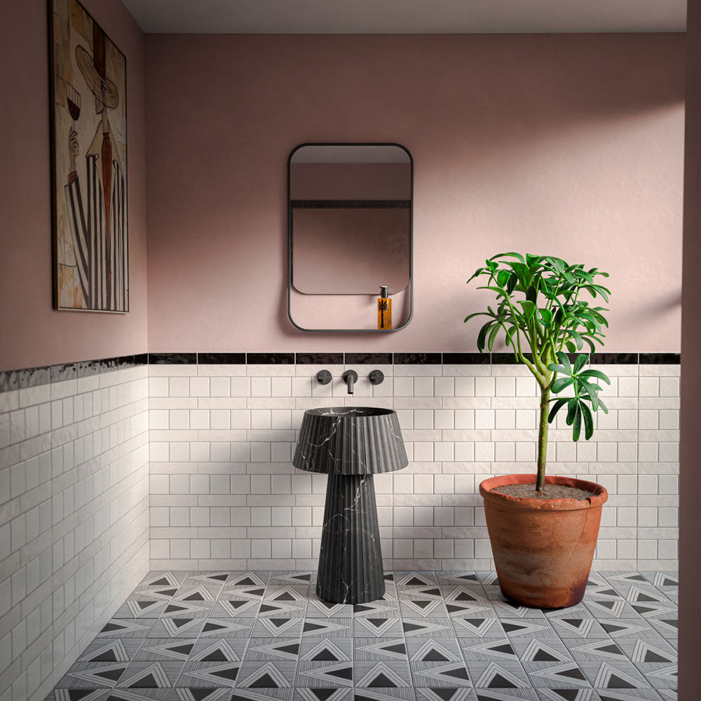 Bathroom featuring Almeira Giza Moroccan style wall and floor tiles in 20cm x 20cm, showcasing a grey and white geometric patterned floor, white brick wall tiles with a black marble border, blush pink walls, a black fluted marble pedestal basin and terracotta planter for a contemporary Moroccan-inspired interior.