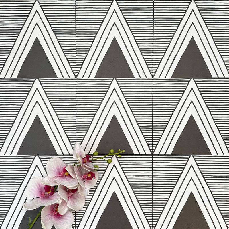 Almeria Giza Moroccan-style porcelain wall and floor tiles arranged in a repeating black and white geometric triangle pattern, 20x20cm, styled with decorative flowers for a striking display.