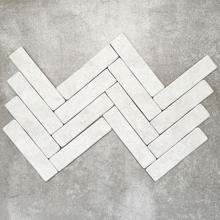 Product image of Amalfi Brick Carrara Vintage Marble wall and floor tiles in a 5.4cm x 22cm format, arranged in a herringbone pattern, showcasing a soft white marble effect surface with subtle tonal variation.
