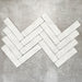 Product image of Amalfi Brick Carrara Vintage Marble wall and floor tiles in a 5.4cm x 22cm format, arranged in a herringbone pattern, showcasing a soft white marble effect surface with subtle tonal variation.