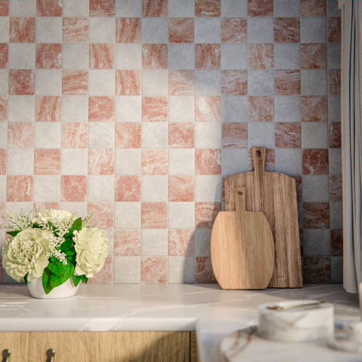 Kitchen setting featuring Amalfi Square Carrara and Rouge 11x11cm vintage marble wall and floor tiles, laid in a chequerboard layout, showcasing soft white and warm terracotta tones, styled with wooden boards, marble worktops and fresh flowers.