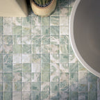 Bathroom featuring Amalfi Square Salvia 11x11cm vintage marble-effect wall and floor tiles, styled with a freestanding bath, brass fixtures, and soft green glazed wall tiles for a serene Mediterranean-inspired space.
