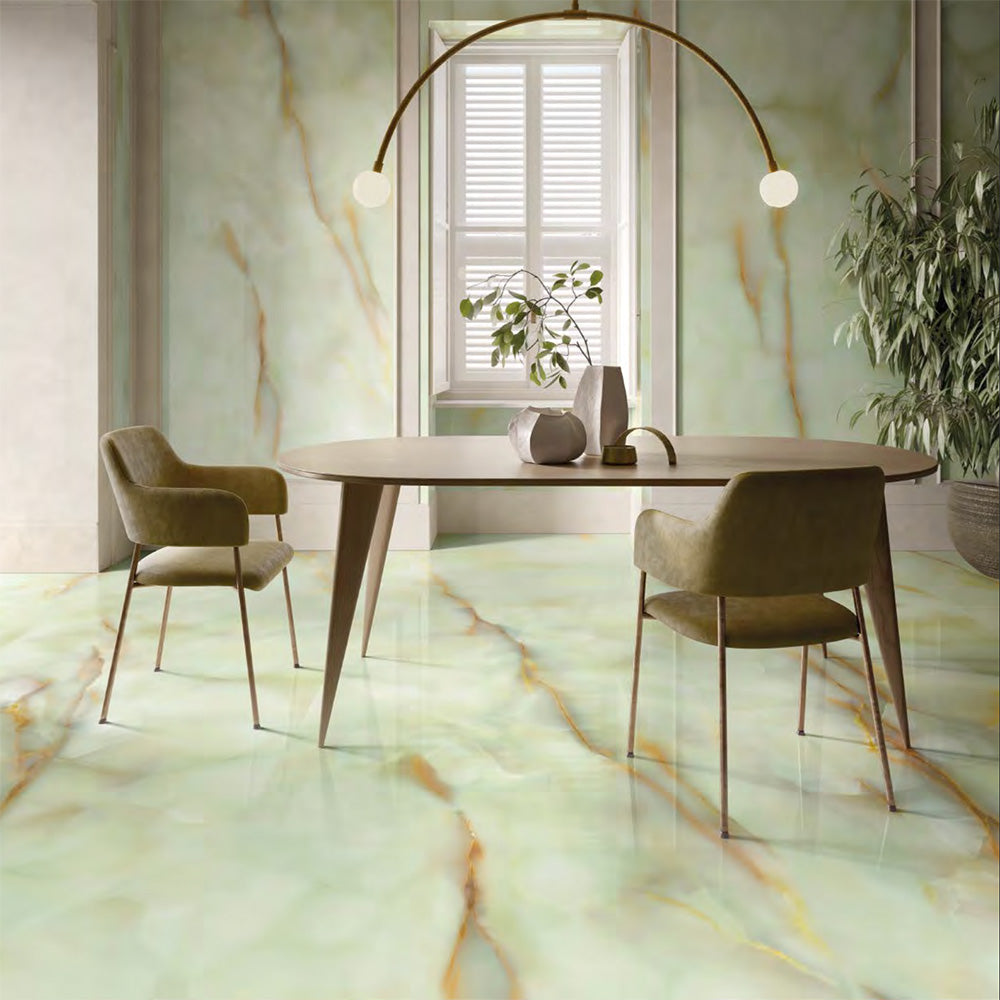 Dining room featuring Anastasia Jade Green Onyx Matt 60 × 120cm stone effect floor and wall tiles, with soft green tones and flowing gold veining, paired with a wooden table, upholstered chairs, and statement lighting.
