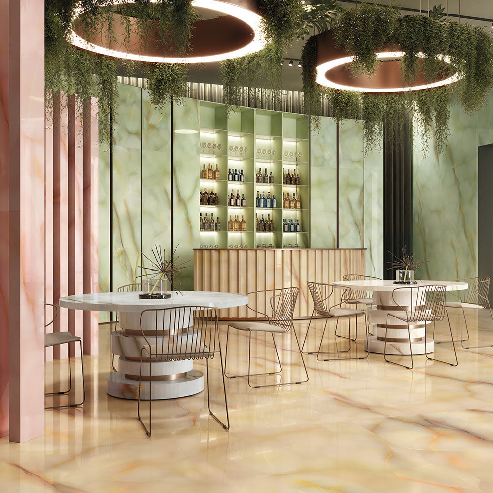 Restaurant interior featuring Anastasia Miele Onyx Matt 60 × 120cm stone effect floor and wall tiles, with warm honey tones and soft veining, paired with curved tables, metallic chairs, green panels, and statement lighting.