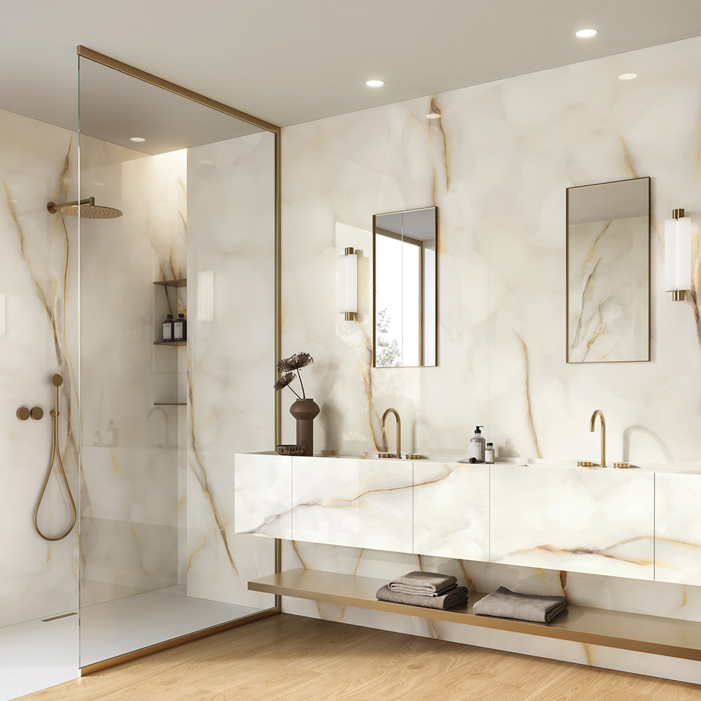 Bathroom interior featuring Anastasia Pearl Onyx Matt 60 × 120cm stone effect wall tiles, with soft cream tones and subtle gold veining, paired with brass fittings, a floating vanity, glass shower enclosure, and warm wood flooring.