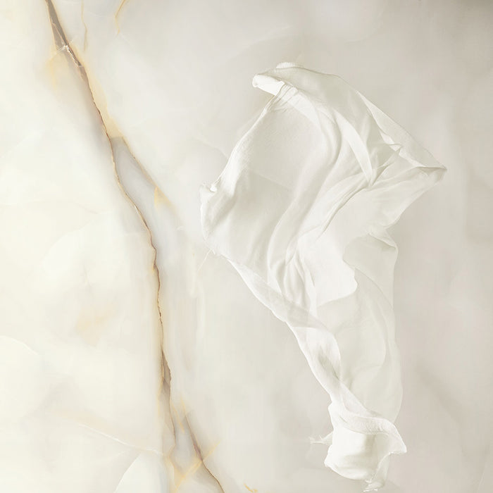 Close-up of Anastasia Pearl Onyx Matt 60 × 120cm stone effect tiles, showcasing soft cream tones with delicate gold veining, styled with a flowing white fabric to highlight the surface texture and elegant finish.