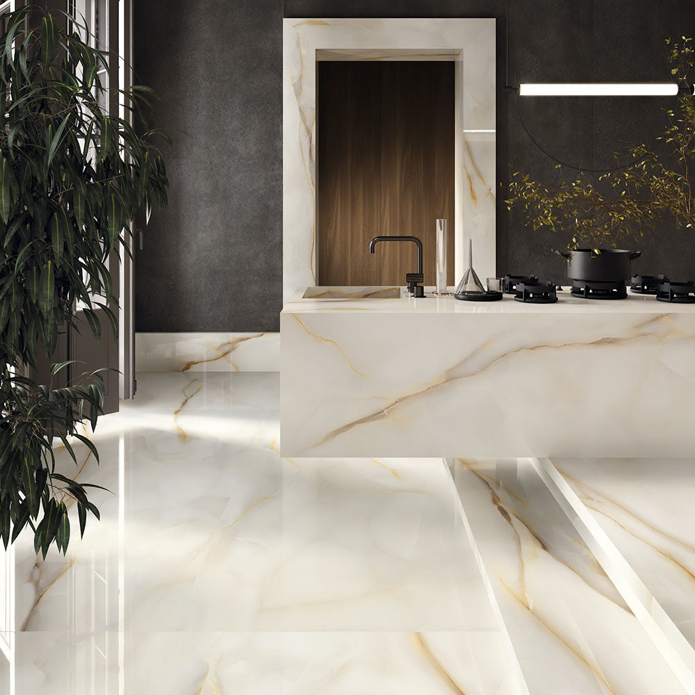 Kitchen interior featuring Anastasia Pearl Onyx Polished 60 × 120cm stone effect floor tiles, with soft cream tones and flowing gold veining, paired with a waterfall island, dark walls, and black fittings for contrast.