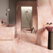 Bathroom interior featuring Anastasia Rose Onyx Matt 60 × 120cm stone effect wall and floor tiles, with soft pink tones and delicate gold veining, paired with a freestanding bath, walk-in shower, and warm brass fittings.