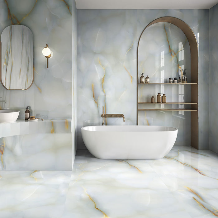 Bathroom interior featuring Anastasia Turchese Blue Onyx Matt 60 × 120cm stone effect wall and floor tiles, with soft blue tones and flowing gold veining, paired with a freestanding bath, built-in shelving, and brass fittings.