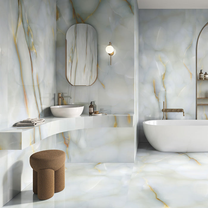 Bathroom interior featuring Anastasia Turchese Blue Onyx Matt 60 × 120cm stone effect wall and floor tiles, with soft blue tones and flowing gold veining, paired with a freestanding bath, built-in shelving, and brass fittings.