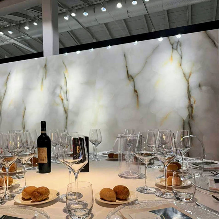 Dining setting featuring Anastasia Turchese Blue Onyx Matt 60 × 120cm stone effect wall tiles, with soft blue tones and flowing gold veining, paired with a dressed table, glassware, and warm overhead lighting.
