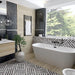 Bathroom interior featuring Art Deco Black & White marble effect patterned porcelain tiles 44 × 44cm, used across the floor and bath panel to create a bold, continuous geometric layout. The contrasting black and white tones introduce strong structure and rhythm, balanced with wood-effect wall panels, a freestanding bath, and matte black fittings for a clean, modern finish.