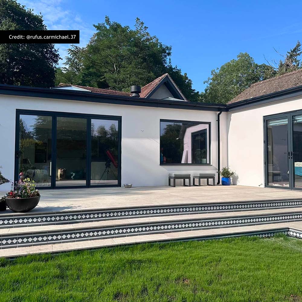 Modern outdoor patio featuring Aston Manor Victorian style border tiles in 20cm x 20cm. Decorative black and white Victorian style border tiles frame the step edges, complementing large stone effect porcelain patio tiles and a contemporary garden design.