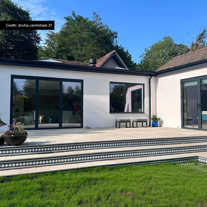 Modern outdoor patio featuring Aston Manor Victorian style border tiles in 20cm x 20cm. Decorative black and white Victorian style border tiles frame the step edges, complementing large stone effect porcelain patio tiles and a contemporary garden design.