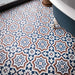 Close-up of Balthazar Grand 20x20cm Victorian and Moroccan-style patterned bathroom floor tiles, featuring intricate geometric and floral motifs in navy blue, terracotta and white, beside a freestanding bathtub.