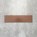 Baroque Cotto porcelain wall and floor tile in a 9.1cm x 37.5cm format, featuring a warm terracotta metallic finish with gently distressed edges, displayed against a textured concrete-effect background.