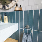 Baroque Laguna Blue 9.1cm x 37.5cm porcelain tiles, showcasing their rich blue finish in a vertical layout, paired with crisp white wall tiles, a pale blue basin and chrome details.