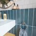 Baroque Laguna Blue 9.1cm x 37.5cm porcelain tiles, showcasing their rich blue finish in a vertical layout, paired with crisp white wall tiles, a pale blue basin and chrome details.