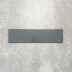 Baroque Laguna Blue porcelain wall and floor tile in a 9.1cm x 37.5cm format, featuring a deep blue metallic finish with gently distressed edges, displayed against a textured concrete-effect background.