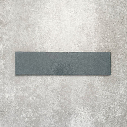 Baroque Laguna Blue porcelain wall and floor tile in a 9.1cm x 37.5cm format, featuring a deep blue metallic finish with gently distressed edges, displayed against a textured concrete-effect background.