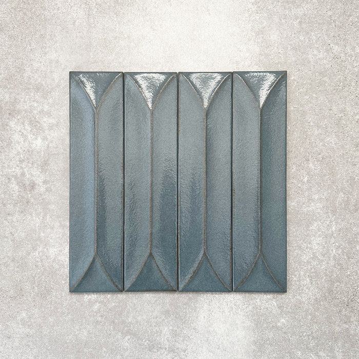 Baroque Decor Laguna Blue porcelain wall tile in a 9.1cm x 37.5cm format, featuring a deep blue metallic finish with a raised geometric relief design and gently distressed edges, displayed against a textured concrete-effect background.