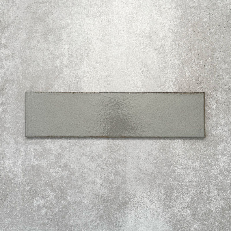 Baroque Lichen Green porcelain wall and floor tile in a 9.1cm x 37.5cm format, featuring a soft sage green metallic finish with gently distressed edges, displayed against a textured concrete-effect background.