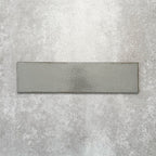 Baroque Lichen Green porcelain wall and floor tile in a 9.1cm x 37.5cm format, featuring a soft sage green metallic finish with gently distressed edges, displayed against a textured concrete-effect background.