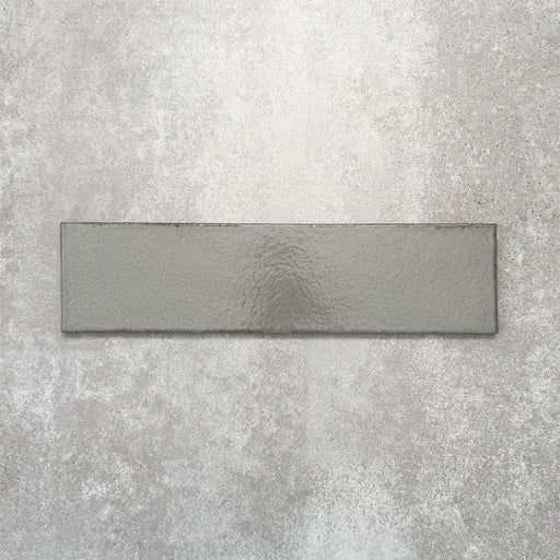 Baroque Lichen Green porcelain wall and floor tile in a 9.1cm x 37.5cm format, featuring a soft sage green metallic finish with gently distressed edges, displayed against a textured concrete-effect background.