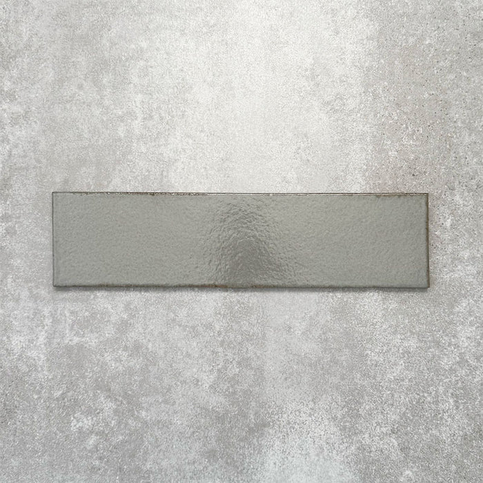 Baroque Lichen Green porcelain wall and floor tile in a 9.1cm x 37.5cm format, featuring a soft sage green metallic finish with gently distressed edges, displayed against a textured concrete-effect background.