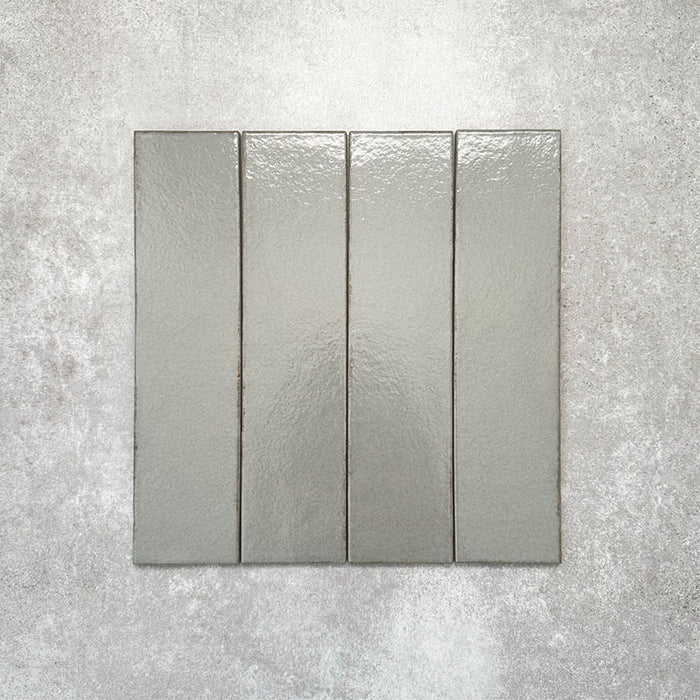 Baroque Lichen Green porcelain wall and floor tile in a 9.1cm x 37.5cm format, featuring a soft sage green metallic finish with gently distressed edges, displayed against a textured concrete-effect background.