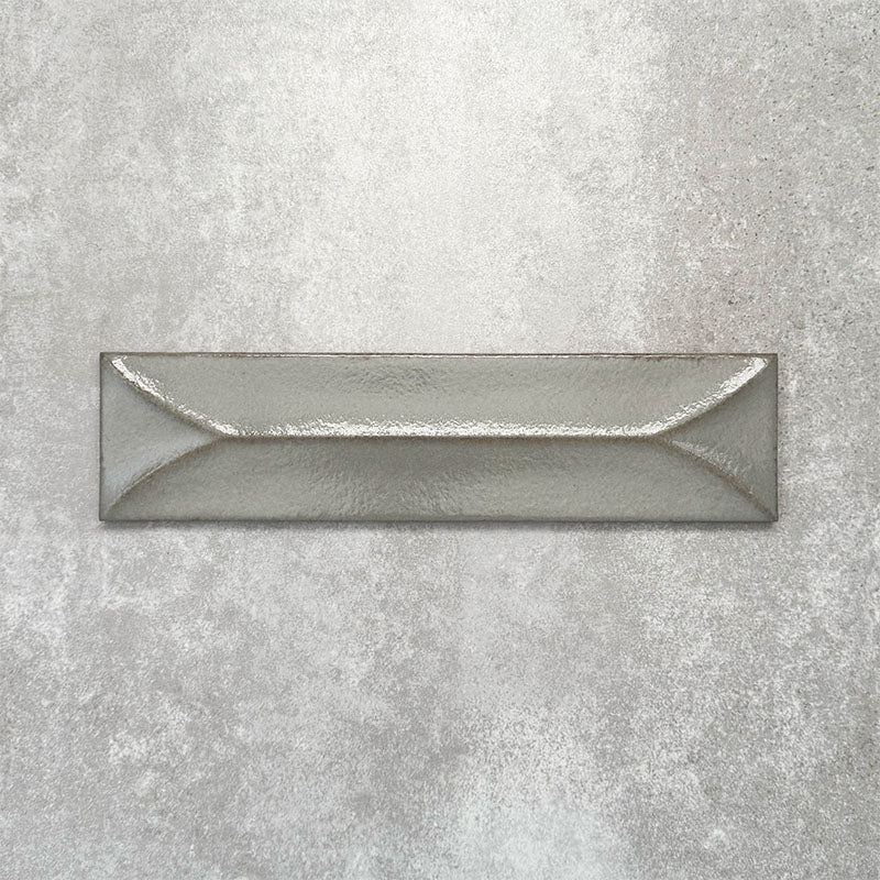 Baroque Decor Lichen Green porcelain wall tile in a 9.1cm x 37.5cm format, featuring a soft sage green metallic finish with a raised geometric relief design and gently distressed edges, displayed against a textured concrete-effect background.