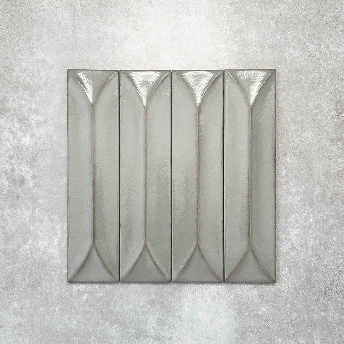 Baroque Decor Lichen Green porcelain wall tile in a 9.1cm x 37.5cm format, featuring a soft sage green metallic finish with a raised geometric relief design and gently distressed edges, displayed against a textured concrete-effect background.