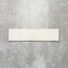 Baroque Vanilla porcelain wall and floor tile in a 9.1cm x 37.5cm format, featuring a soft cream metallic finish with gently distressed edges, displayed against a textured concrete-effect background.