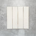 Baroque Vanilla porcelain wall and floor tile in a 9.1cm x 37.5cm format, featuring a soft cream metallic finish with gently distressed edges, displayed against a textured concrete-effect background.