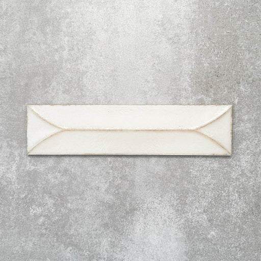 Baroque Decor Vanilla porcelain wall tile in a 9.1cm x 37.5cm format, featuring a soft cream metallic finish with a raised geometric relief design and gently distressed edges, displayed against a textured concrete-effect background.