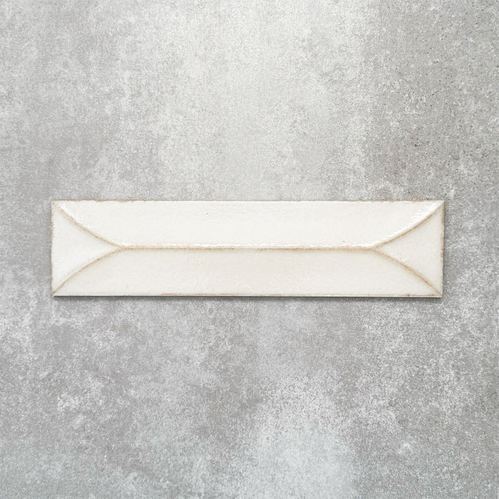 Baroque Decor Vanilla porcelain wall tile in a 9.1cm x 37.5cm format, featuring a soft cream metallic finish with a raised geometric relief design and gently distressed edges, displayed against a textured concrete-effect background.
