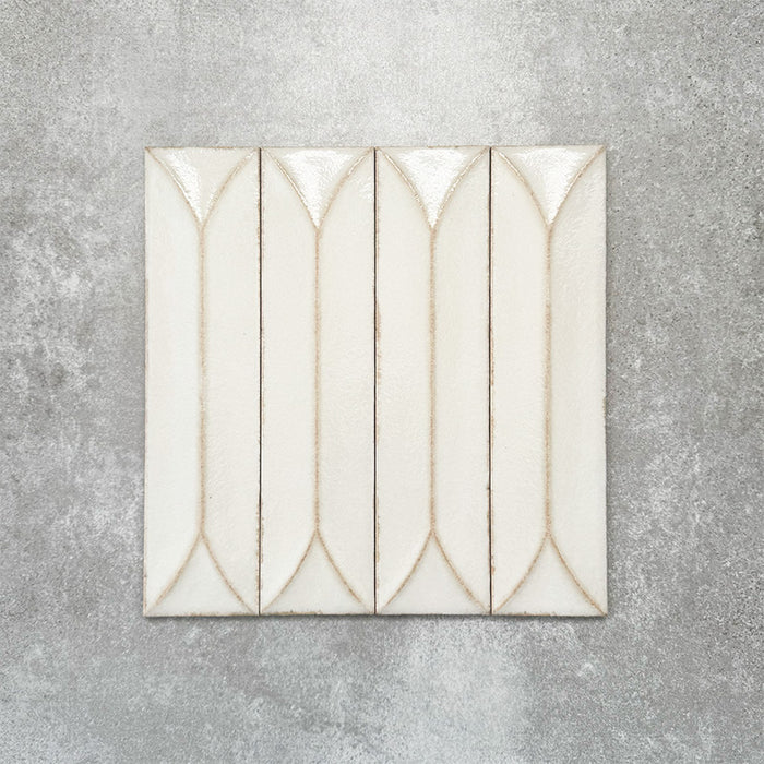 Baroque Decor Vanilla porcelain wall tile in a 9.1cm x 37.5cm format, featuring a soft cream metallic finish with a raised geometric relief design and gently distressed edges, displayed against a textured concrete-effect background.