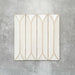 Baroque Decor Vanilla porcelain wall tile in a 9.1cm x 37.5cm format, featuring a soft cream metallic finish with a raised geometric relief design and gently distressed edges, displayed against a textured concrete-effect background.