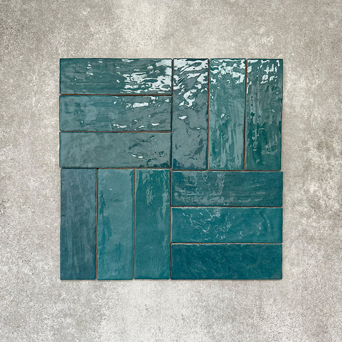 Flat lay of Zellige Peacock Green 6.5×20cm Moroccan-style ceramic brick tiles, shown in a basketweave layout, showcasing deep blue-green tones, a glossy handmade-look glaze and natural tonal variation on a neutral background.