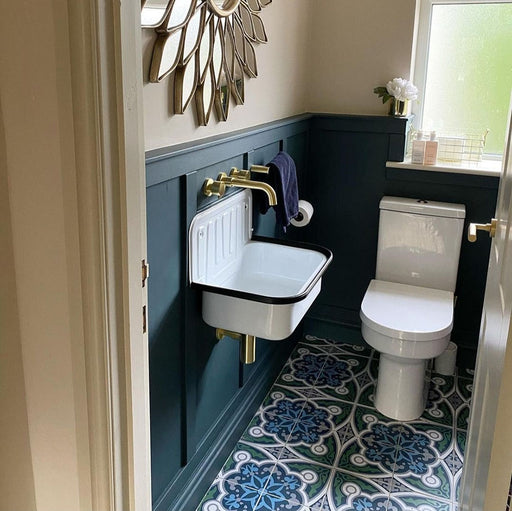 Bathroom interior featuring London Streets Baker Street 20x20cm Victorian Moroccan style floor tiles, styled with deep blue wall panelling, brass fittings and a compact wall-mounted sink, creating a bold patterned bathroom floor.