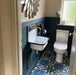 Bathroom interior featuring London Streets Baker Street 20x20cm Victorian Moroccan style floor tiles, styled with deep blue wall panelling, brass fittings and a compact wall-mounted sink, creating a bold patterned bathroom floor.