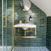 Bathroom featuring Zellige Royal Green Brick 6.5 × 20cm Moroccan-style ceramic wall tiles in rich deep green tones, laid in a horizontal brick layout around a wall-mounted basin, paired with brass fittings, a glass shower screen and patterned floor tiles for a bold, elegant zellige-effect finish.