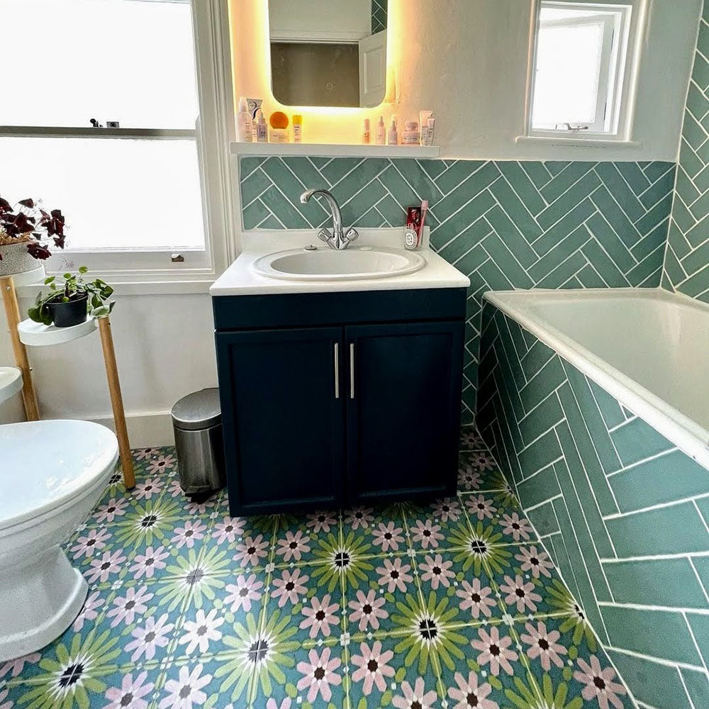 Bathroom floor featuring Fez Summer 20x20cm Moroccan-style porcelain tiles, showcasing a colourful geometric star pattern in soft green, blue and blush pink tones, paired with green herringbone wall tiles, a dark vanity unit and white bathroom fixtures for a fresh, characterful look.