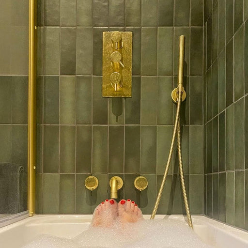 Bathroom featuring Zellige Malachite Green 6.5×20cm Moroccan-style ceramic brick tiles, installed on the walls around a bath and shower, paired with brushed brass fittings, a wooden vanity unit and a stone basin for a warm, spa-like finish.