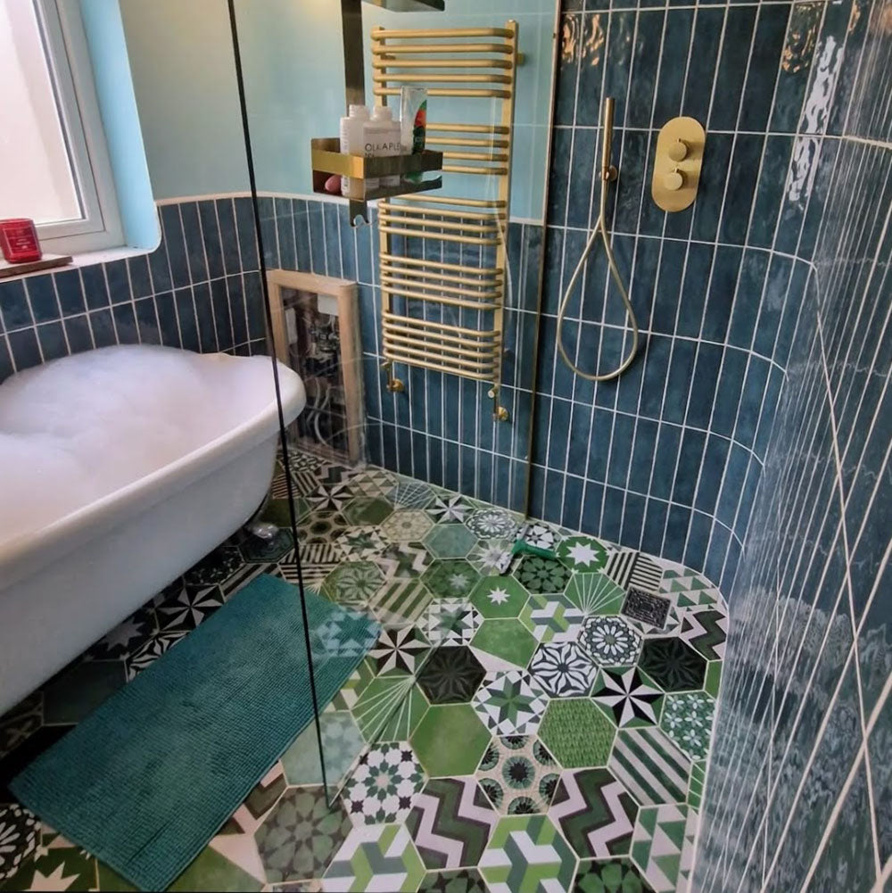 Bathroom featuring Fayrouz Verde Hexagon Patchwork Moroccan-style porcelain tiles in an 18.7×21.6cm hexagon format, combining intricate geometric and star patterns in layered green, sage and charcoal tones, paired with deep blue glazed wall tiles, brushed brass fixtures and a curved walk-in shower for a bold, character-led finish.