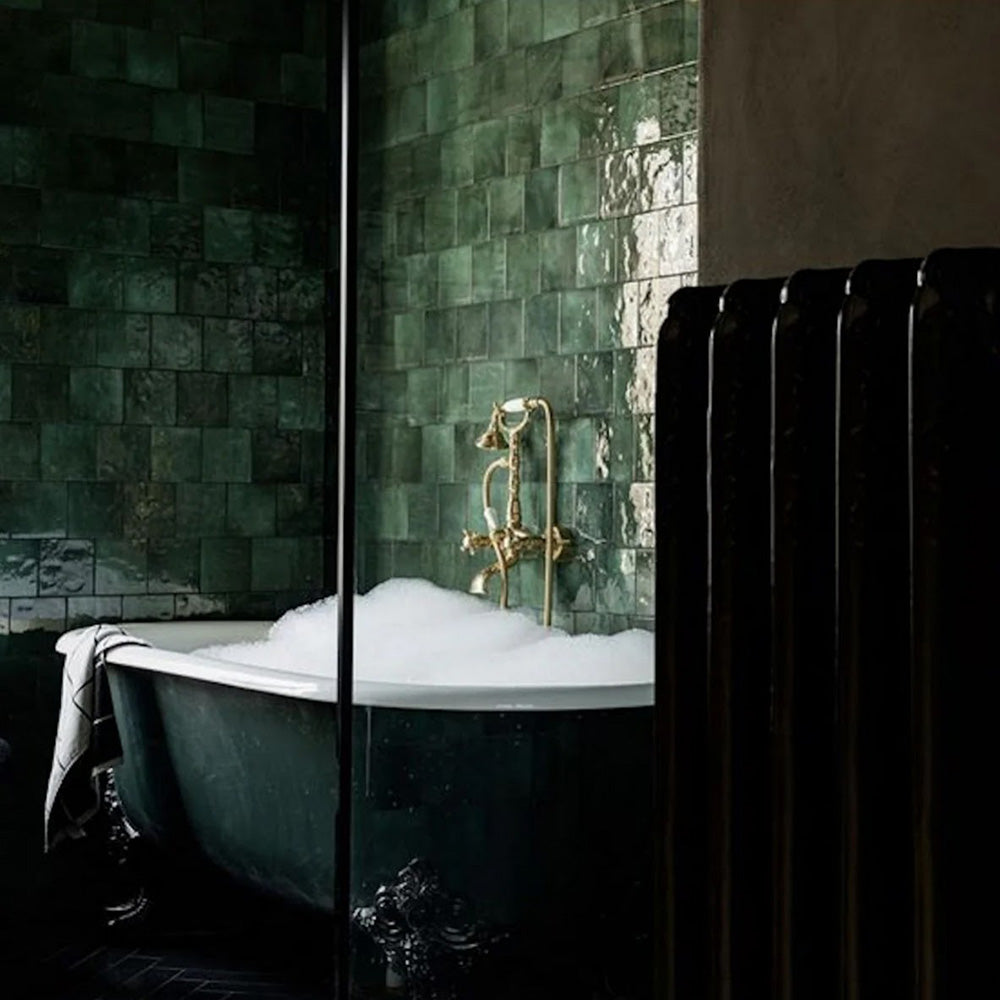 Bathroom featuring Zellige Royal Green Square 13.2 × 13.2cm Moroccan-style ceramic wall tiles in rich deep green tones, laid in a classic grid around a freestanding bath with brass fittings, creating a dramatic, moody and handcrafted zellige-effect finish.