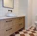 Bathroom interior featuring Fayrouz Rosso 15.2x15.2cm natural marble tiles with a tumbled finish, installed in a chequerboard floor with light marble, styled with a wooden vanity unit, round basin and neutral walls.