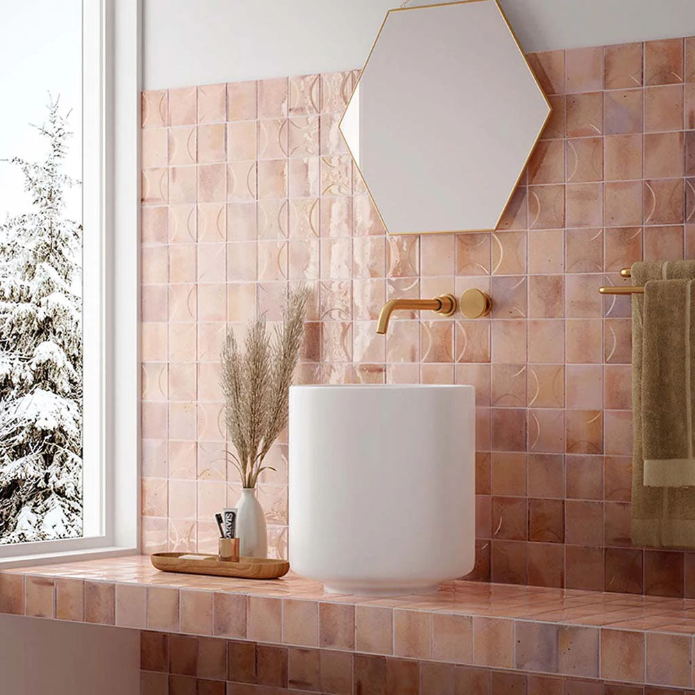 Bathroom vanity splashback featuring Saigon Rose Pink Decor Square Wall tiles in a Moroccan-inspired style, 10 × 10cm glossy ceramic tiles in soft blush and rose tones with a decorative relief pattern, paired with brass fittings and a hexagonal mirror.