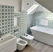 Bathroom interior featuring Agadir Green Moroccan-style 20x20cm porcelain wall tiles, showcasing a repeating geometric star pattern in green and white, styled with a freestanding bath, modern sanitaryware and a bright, airy layout.